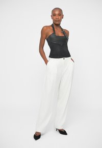 Top de halter em couro preto com design ajustado, combinado com calças brancas risca de giz e sapatos de salto preto com bico fino. Textura suave, forma estruturada.