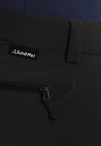 Shorts noirs en tissu lisse, avec une poche zippée sur le côté et une étiquette à la taille affichant le nom de la marque "Schöffel."