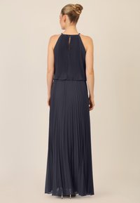 Abito maxi plissettato blu navy scuro con scollo a halter e dettaglio a chiave sulla schiena. Realizzato in tessuto leggero, scivola elegantemente dai fianchi.