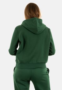 Grøn hættetrøje med hætte, ribbede manchetter og talje. Glat stof med en tætsiddende design, synlige sømme, og uden mønstre eller accenter.
