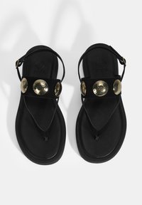 Schwarze Flip-Flop-Sandalen mit einem strukturierten oberen Riemen, der drei runde, gehämmerte goldene Akzente aufweist. Die Sohle ist glatt und flach.