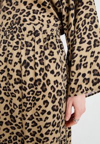 Leopardmønstret plagg i beige stof har en afslappet pasform med elastisk talje og lette ærmer, der fremhæver en glat tekstur.