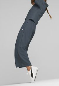 Dark gray athletic outfit featuring a short-sleeve top and wide-leg pants, made of textured fabric, paired with white and black sneakers.