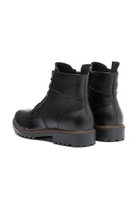 Botas de cuero negro hasta el tobillo con superficie texturizada, punta redondeada, suela de goma resistente y detalle de costura marrón alrededor de la suela.