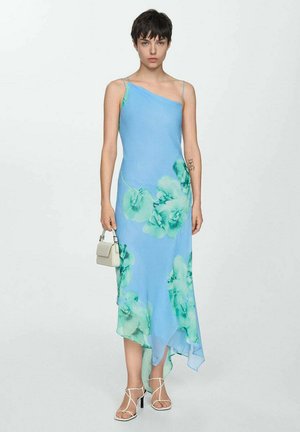 Asymmetrical blue dress with green floral print, lightweight fabric, spaghetti straps, and a fluid silhouette. Worn with white strappy sandals.