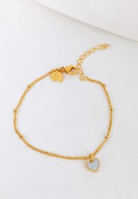 Pulsera de cadena de tono dorado con pequeños acentos redondos y un colgante en forma de corazón que presenta un brillo arcoíris. Cierre ajustable y cadena de extensión.
