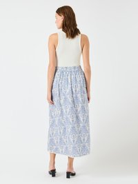 Un maiou alb cu dungi, asociat cu o fustă lungă cu model albastru și alb. Fusta prezintă design floral și o talie plisată. Pantofi negri cu toc gros.