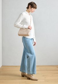 Beige lædertaske med rektangulær form og frontlomme, parret med en hvid ribbet skjorte og lyseblå brede jeans.