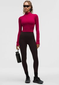 Pielāgota, garām piedurknēm, rozā krāsā ar rāvējslēdzēju; augstās melnās legingi; melna ūdens pudele; melnas sporta kurpes ar teksturētām zolēm.