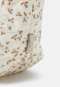 Quiltet stoffveske med beige bakgrunn og brun blomstermønster. Har et lite merkelapp; myk tekstur og avrundet form.