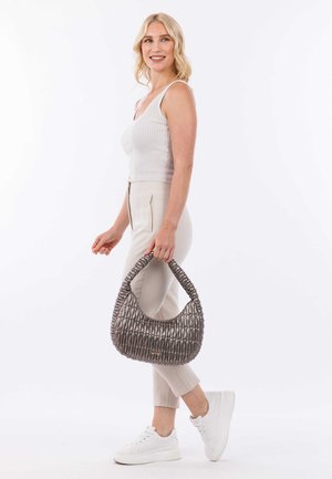 Sac à main texturé gris avec un design tissé, doté d'une poignée épaisse. Une personne portant un haut côtelé et un pantalon beige tient le sac de manière décontractée.