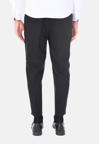 Pantaloni neri con una vestibilità su misura, caratterizzati da una texture liscia e pieghe, abbinati a eleganti scarpe nere lucide.