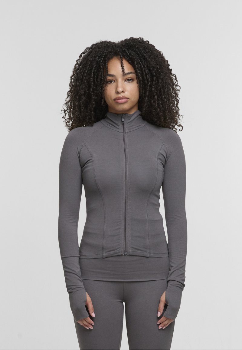 Veste de sport gris à manches longues avec fermeture éclair, col montant, coupe ajustée et passages pour les pouces aux poignets ; tissu lisse et extensible.