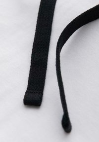 Dvě černé šňůrky od bot spočívající na bílém látkovém pozadí, jedna leží rovně a druhá se zakřivuje nahoru.