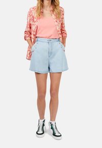 Ljusblå denimshorts med broderade blommor, kombinerade med en korallfärgad linne och en mönstrad rosa skjorta. Vita och gröna hög-top sneakers.