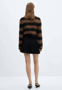 Bruine en zwarte gestreepte mohair trui, gecombineerd met een zwarte geplooide rok. De outfit heeft een zachte textuur en een aansluitende silhouette.