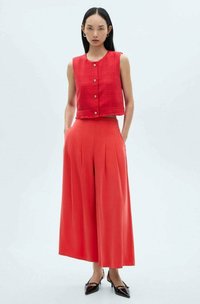Rode gecropte vest met knoopsluiting en een rafelige onderrand, gecombineerd met brede broekspijpen, ook in het rood, met plooien en elegante zwarte hakken.