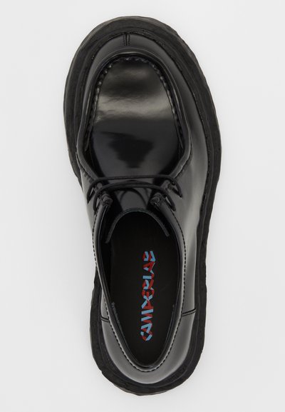 Zapato de cuero negro con superficie brillante, punta redonda, suela de goma texturizada en contraste y cordones negros. En el interior presenta un logotipo colorido.