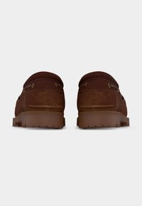 Καφέ μοκασίνια από σουέντ με παχιές λαστιχένιες σόλες, σε προβολή από πίσω, σε λευκό απλό φόντο.