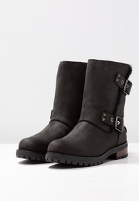 Černé semišové kotníkové boty s kulatou špičkou, plochou gumovou podrážkou a stříbrnými přezkami po straně. Hladký povrch a nízký střih.