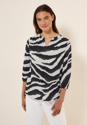 Blusa a rayas en blanco y negro con mangas tres cuartos, escote en V y tejido suave y texturizado. Combinada con pantalones blancos.