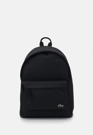 Sac à dos noir en tissu résistant, avec un dessus arrondi, une poche zippée à l'avant et un logo discret sur le devant. Texture lisse.