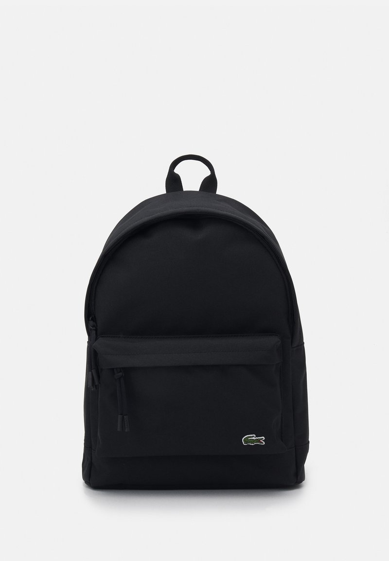 Mochila negra hecha de tejido duradero, con una parte superior curva, bolsillo frontal con cremallera y un logo sutil en la parte delantera. Textura suave.