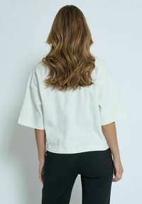 White cotton t-shirt with a boxy fit, dropped shoulders, and a cropped length. Smooth texture and simple design, paired with black pants.