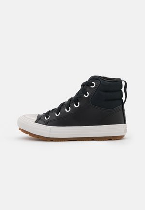Zapatillas altas negras de cuero y lona, con tapa de punta de goma blanca, cordones redondos y suela de goma marrón.
