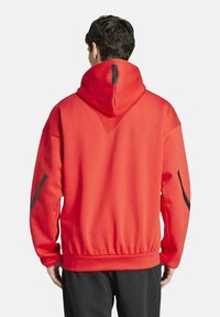 Rode hoodie van textuurmateriaal, oversized ontwerp, verstelbare capuchon en zwarte accentstrepen op de mouwen; elastische tailleband aan de onderkant.