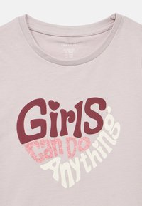 Ανοιχτό ροζ βαμβακερό T-shirt με στρογγυλή λαιμόκοψη, που απεικονίζει μια καρδιά με το γράμμα "Τα κορίτσια μπορούν να κάνουν τα πάντα" με έντονα γράμματα σε διάφορα χρώματα και υφές.