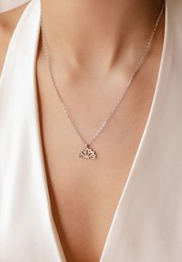 Collier en argent avec un pendentif en fleur de lotus, présentant un design ouvert et une finition lisse, reposant sur un décolleté clair.