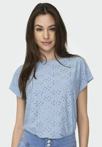 Lyseblå bluse med et struktureret øje-design, korte ærmer og en afslappet pasform. Stoffet har en glat overflade med dekorative udskæringer.
