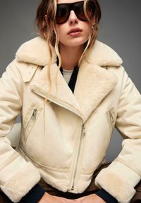 Crème faux shearling bomberjack met ritszakken, sjaalkraag en ribgebreide manchetten. Gekocht met donkere kleding en oversized zonnebril.
