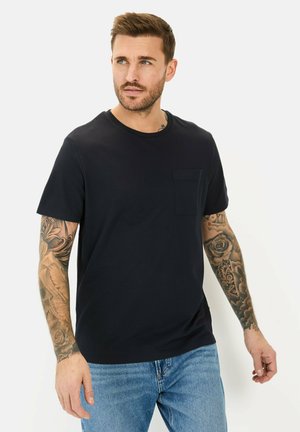 Marineblå t-shirt med rund hals lavet af bomuld, der har korte ærmer og en brystlomme på venstre side. Båret med lyseblå jeans.