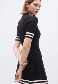 Melna ribota kleita ar piegulošu augšdaļu un izplatušos svārku daļu. Īsajām piedurknēm ir baltas svītras. Aizmugures skats atklāj klasisku polo apkakli.