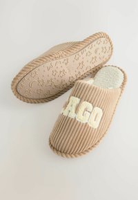 Beige corduroy-luistimet, joissa on uritettu pinta ja pehmeä sisus. Varustettu 'AGO'-kirjaimilla ja kuvioidulla kumipohjalla, jossa on tähtiä ja kuutamoita.