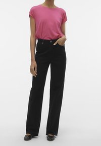 Top rosa a maniche corte abbinato a pantaloni neri a gamba larga a vita alta. Le scarpe ballerine nere completano l'outfit. Tessuto liscio, design informale.