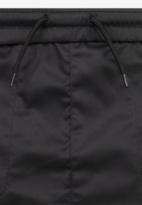 Svarta idrottsshorts med en slät yta, elastisk midja med dragsko och stilren design. Sömdetaljer är synliga.