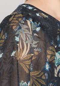 Tessuto nero trasparente con un motivo floreale in blu, verde e beige. Presenta dettagli arricciati lungo lo scollo e una texture morbida.