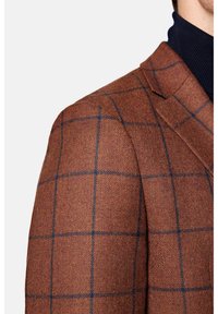 Brązowa marynarka w kratę z niebieskim wzorem, teksturowany materiał, klapy z wycięciem i dopasowany krój. Widoczne szwy oraz detale na szwie ramion.