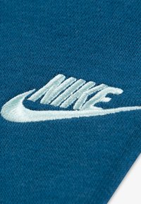 Modrá tkanina s vyšívaným bielym logom Nike, s textúrovaným povrchom a hladkým dokončením, zdôrazňujúca osobitný design značky.