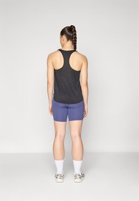 Débardeur noir à dos nageur, shorts violets, chaussettes de sport blanches et baskets de couleur claire. Tissu lisse, coupe ajustée et shorts de longueur mi-cuisse.
