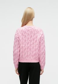 Jersey de punto rosa con un patrón texturizado de burbujas, cuello redondo y dobladillo acanalado. Mangas largas que llegan hasta las muñecas.