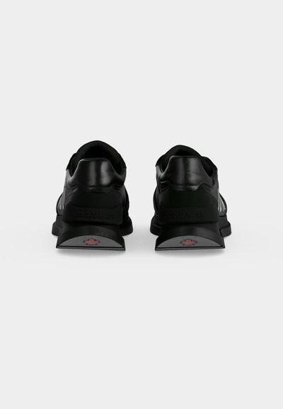 Paire de baskets noires vues de dos avec des talons épais présentant un petit logo de feuille d’érable rouge sur chaque languette de talon.