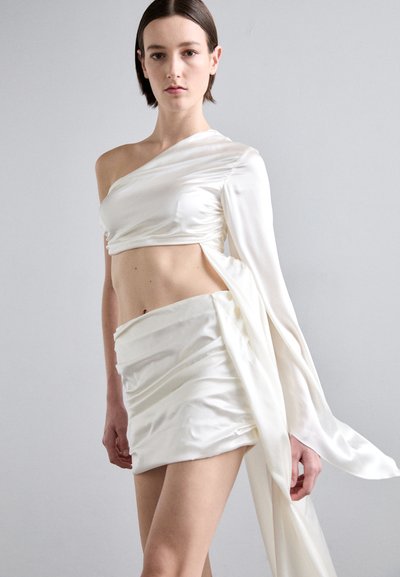Compleu din două piese din satin, care include un top pe un umăr și o fustă înfășurată asimetrică, de culoare albă moale. Textură netedă cu detalii drapate.