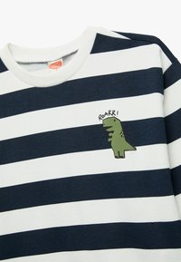 Navy en witte gestreepte sweatshirt van katoen, met een kleine groene dinosaurusschildering en het woord "ROARR!" op de linkerborst.