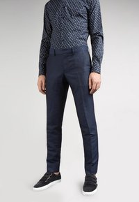 Tmavě námořnické kalhoty slim fit vyrobené z tkané látky. V kombinaci s košilí s potiskem a černými nazouvacími botami.