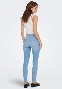 Svetloplave uske traperice visokog struka sa glatkom teksturom, s dva stražnja džepa i ušivenim detaljima, uparene s uskom bijelom majicom bez rukava.