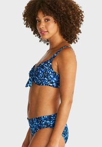 Blå blommig bikinisett som har en rynkad topp med justerbaraaxlar och matchande lågriskade bottnar, båda med ett iögonfallande mönster.